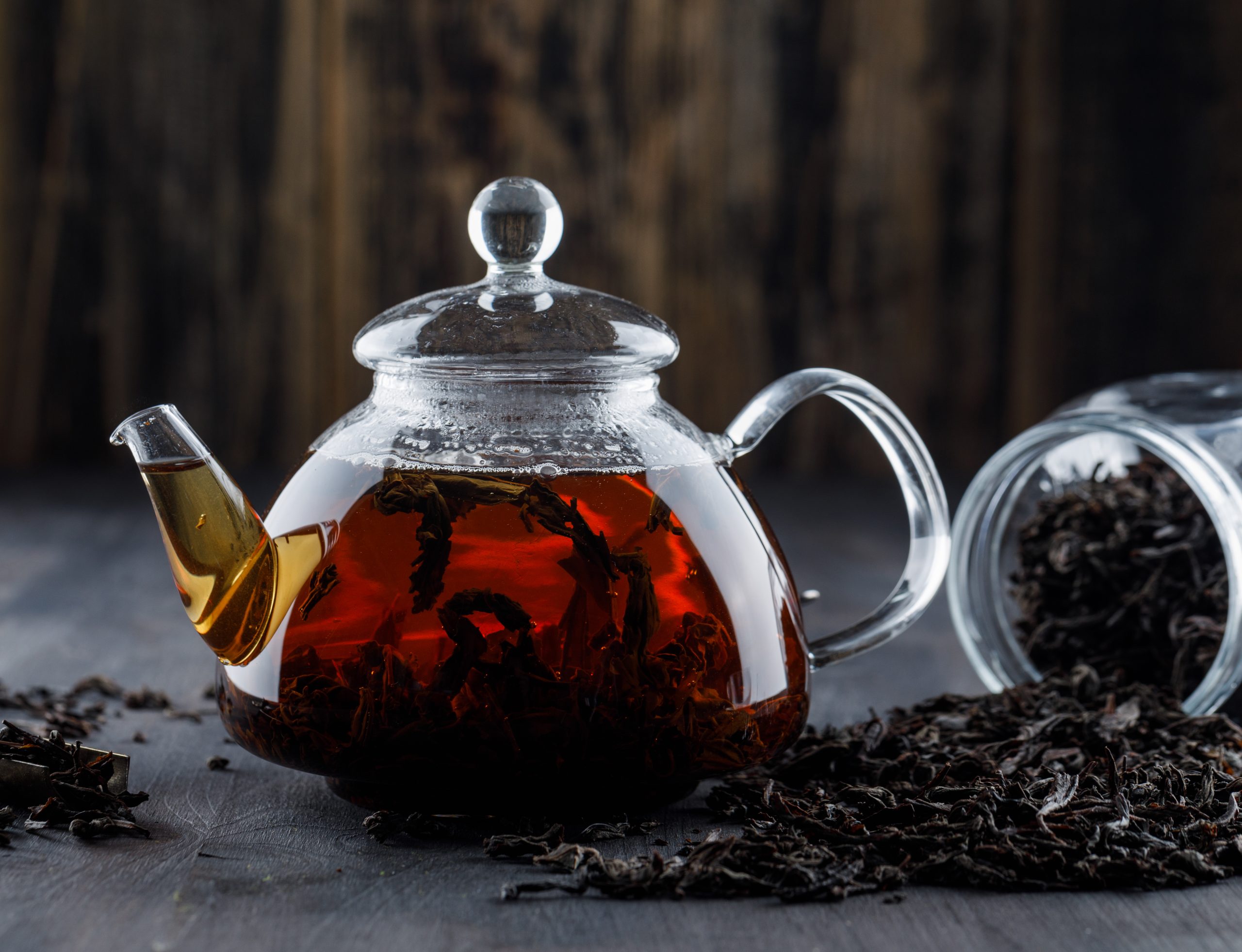 Black tea with dry tea in a teapot on wooden background, side view.